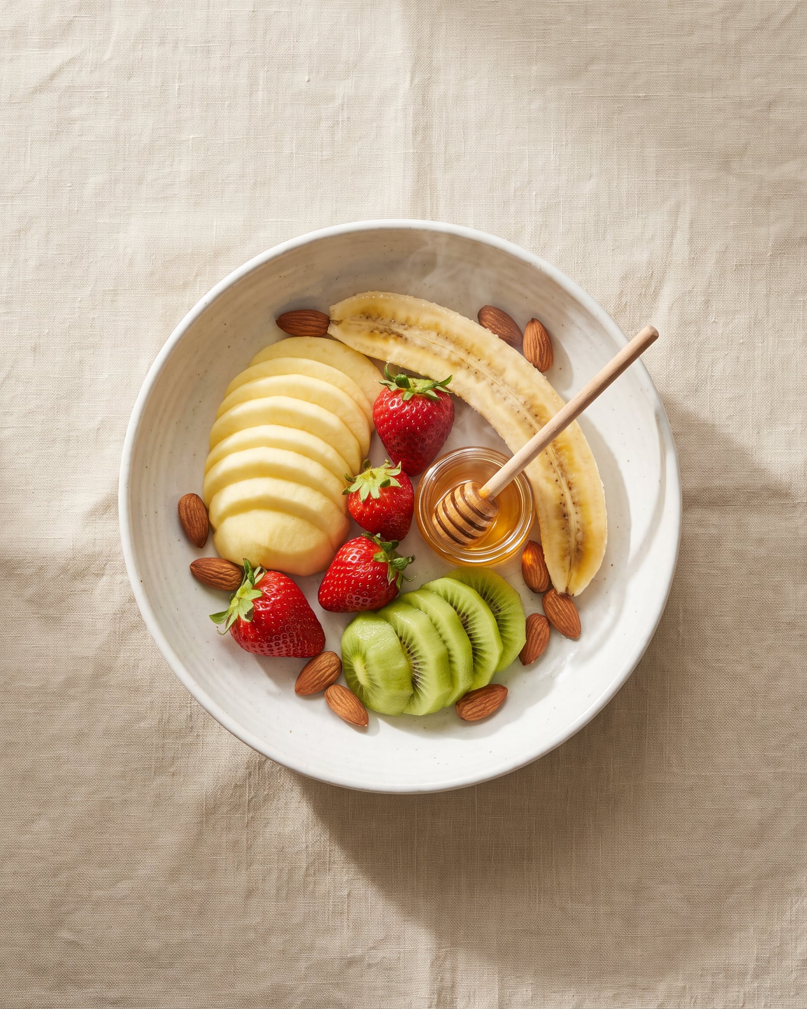 Sliced apple, strawberries, kiwi, banana and almonds with a pot of honey.